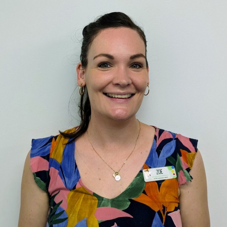 A woman smiling at the camera, wearing a colorful blouse and a nametag labeled "Zoe Jones." She has a necklace and earrings.